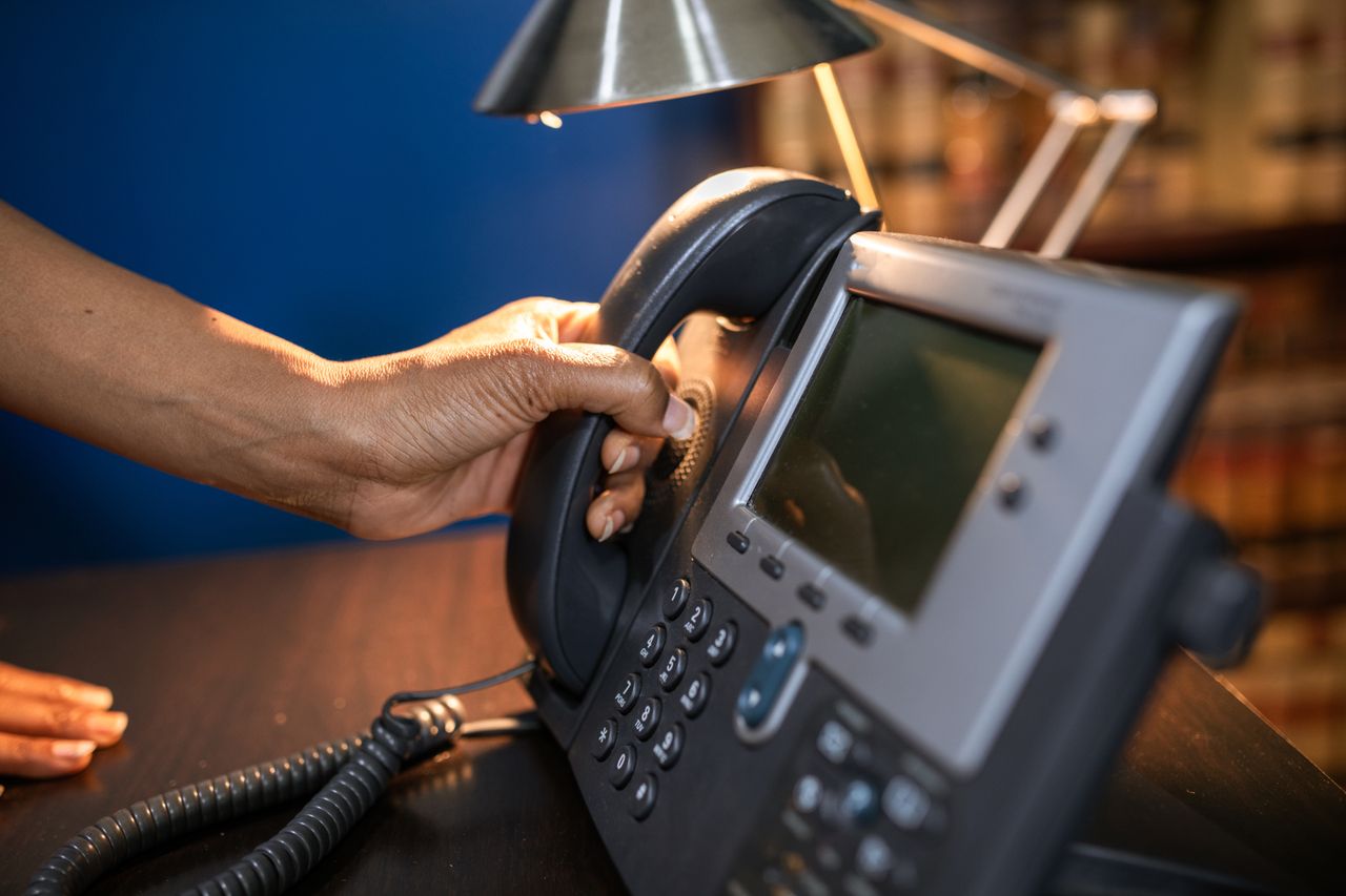 The Art of Drawing Readers In: Your attractive post title goes here A close-up image of a hand picking up a handset from an office telephone, emphasizing communication device usage.